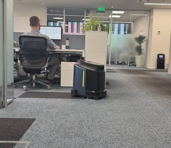 Autonomous cleaning robot working in office environment while person works at desk