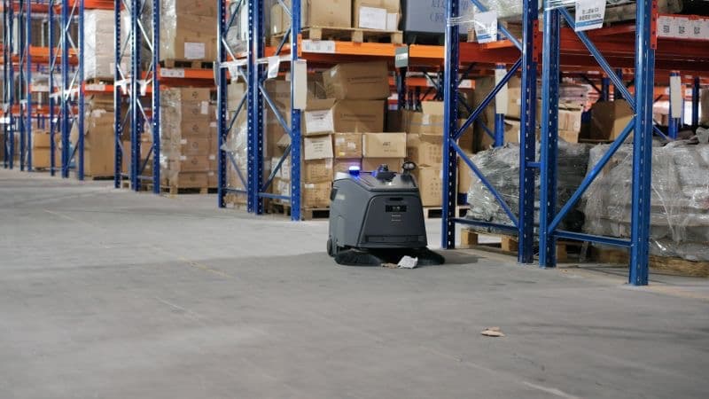 Autonomous cleaning robot working in warehouse with blue racking systems